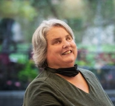 A woman with grey hair, green shirt and bright smile.