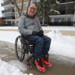 Man in wheelchair on a snowy sidewalk.