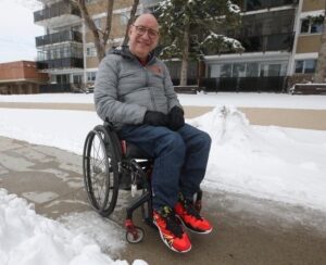 Man in wheelchair on a snowy sidewalk.