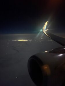The engine and wing of an airplane flying over a city at night