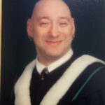 Bald man in black graduation gown