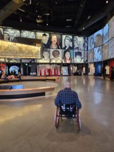 Bald man in a wheelchair in front of a large video disability