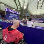 A bald man in a wheelchair watching fencing