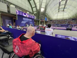 A bald man in a wheelchair watching fencing