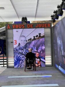 Peter in his wheelchair in front of a large video display