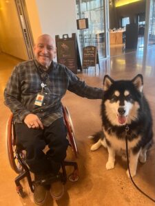 Peter a bald man in a wheelchair is petting a large husky dog