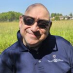 Peter is bald.He is wearing sunglasses and a blue tee.