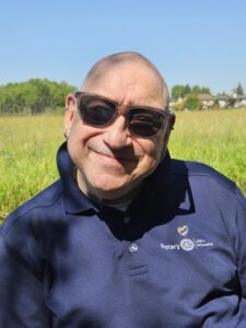 Peter is bald.He is wearing sunglasses and a blue tee.