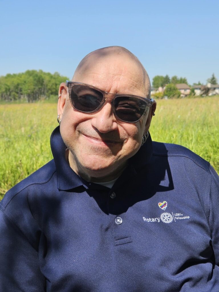 Peter is bald.He is wearing sunglasses and a blue tee.